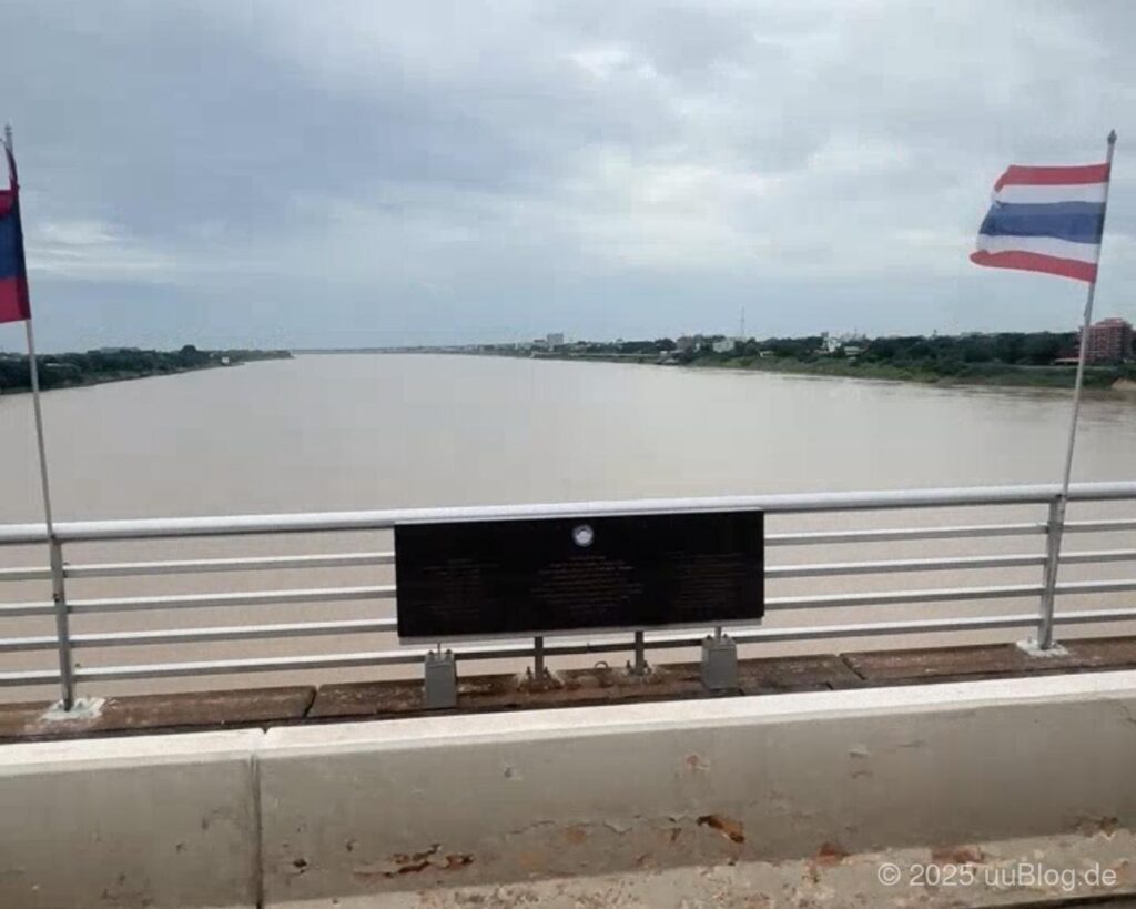 Blick von einer Brücke auf den Mekong mit Flaggen von Laos und Thailand.