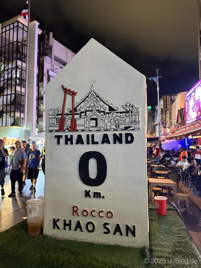 Weißer Meilenstein mit Aufschrift 'Thailand 0 Km' in der Khao San Straße bei Nacht, Bangkok.
