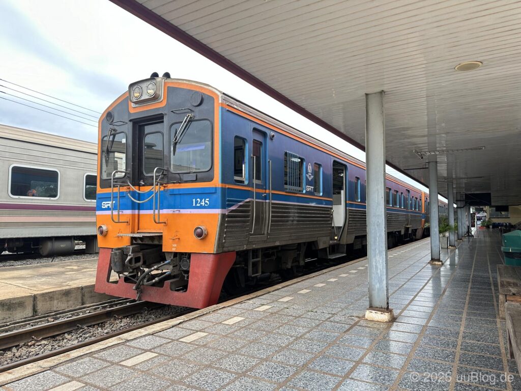 Ein moderner blauer und orangefarbener Zug steht an einem überdachten Bahnsteig in Nong Khai, Thailand.