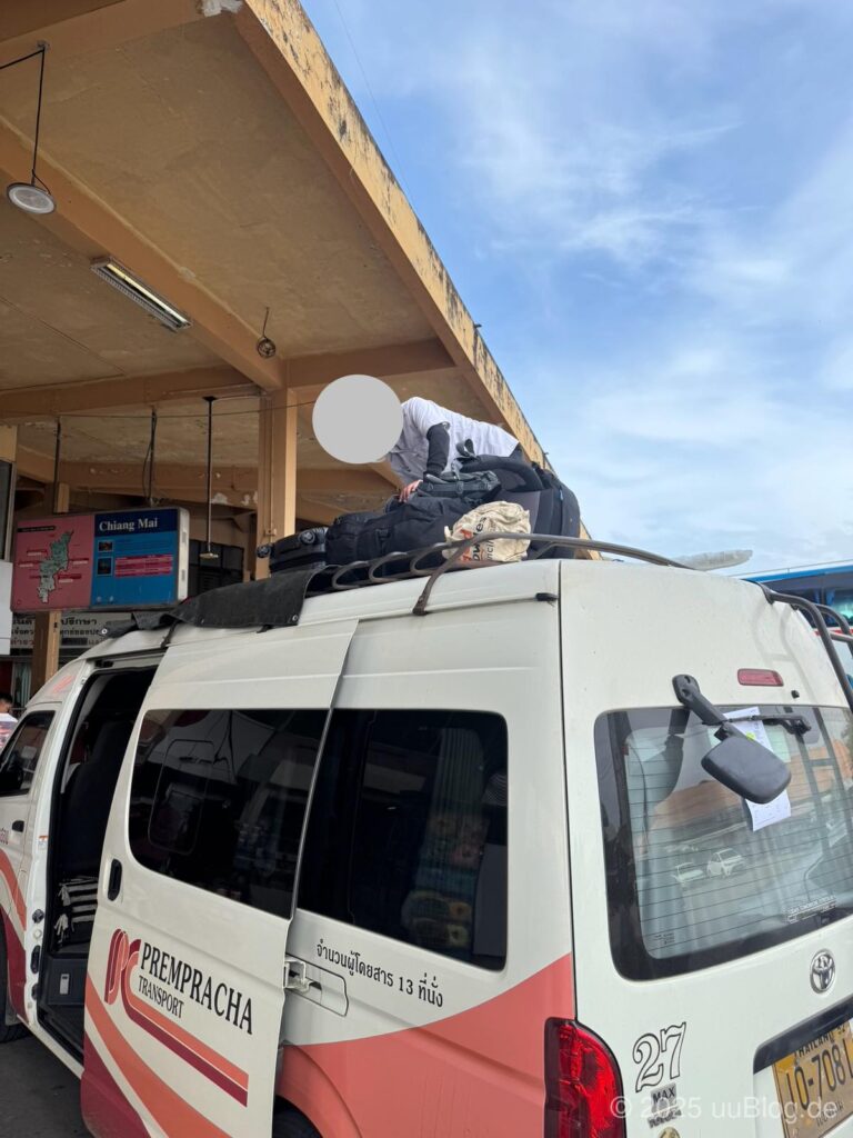 Ein Mann belädt einen Minivan der Prempracha Transport mit Gepäck auf dem Dach.