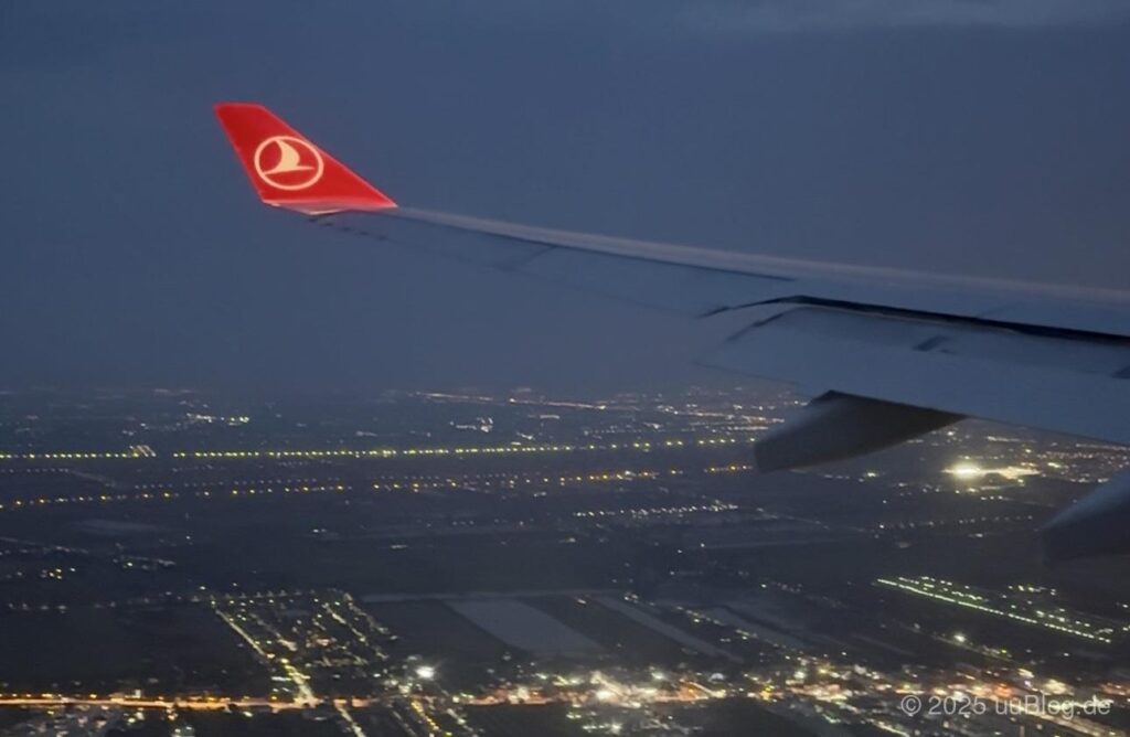 Flugzeugflügel über einer nachts beleuchteten Stadt, aufgenommen aus der Luft.