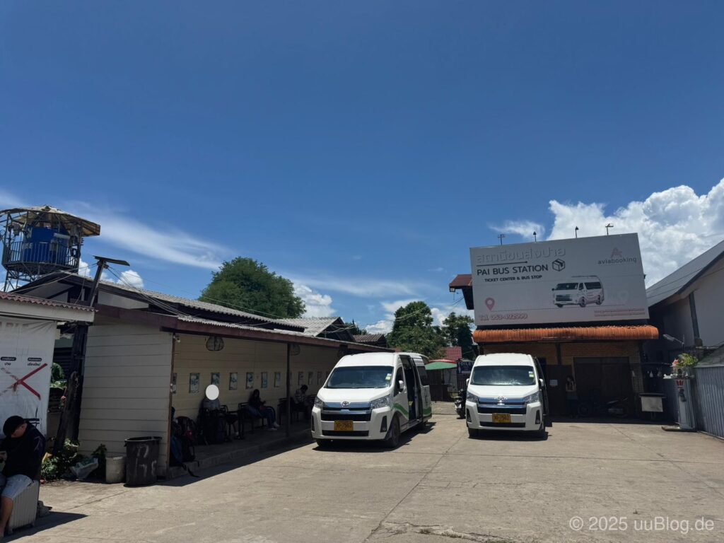 Bushaltestelle in Pai, Thailand mit zwei weißen Minivans unter klarem Himmel.