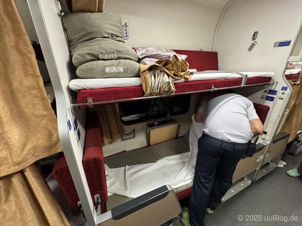 Ein Schlafabteil im Nachtzug in Thailand mit Etagenbett und einem Mitarbeiter, der Bettwäsche ordnet.