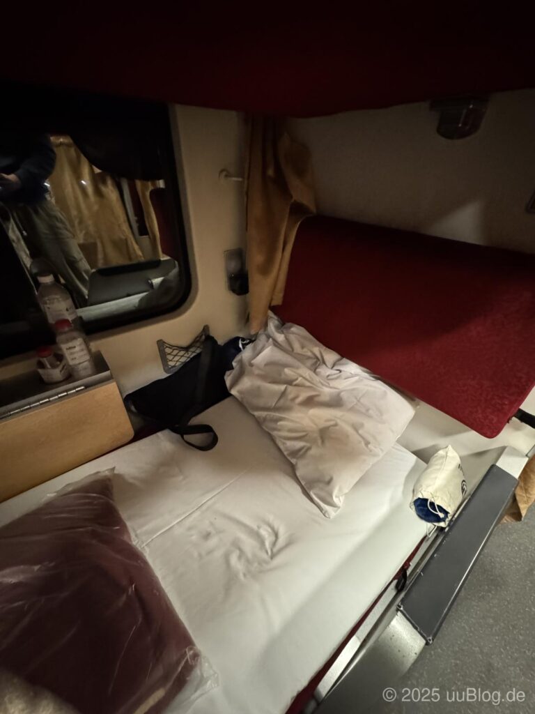 Ein Bett in einem Schlafwagenabteil in Thailand mit roten Vorhängen und weißer Bettwäsche.