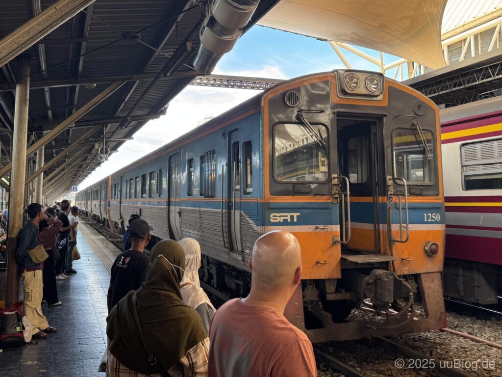 Eine Menschenmenge wartet am Bahnsteig neben einem SRT-Zug in einem thailändischen Bahnhof.