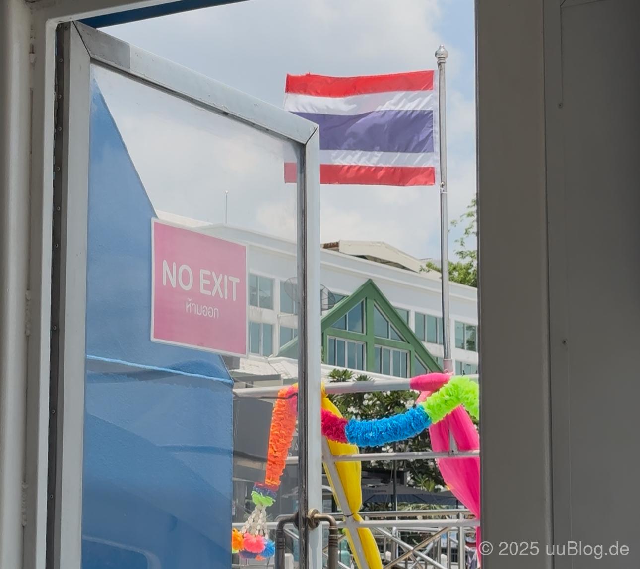 Offene Tür mit Schild 'No Exit' und thailändische Flagge im Hintergrund.
