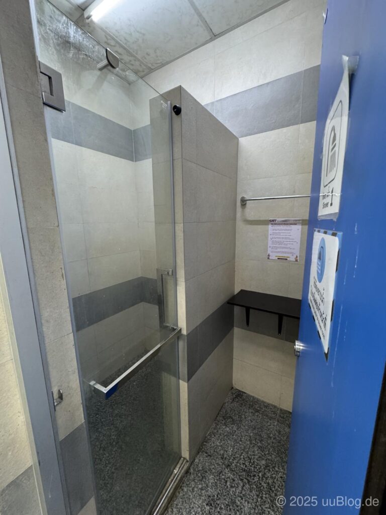 Eine moderne Duschkabine mit grauen Fliesen und Glastür in einem Bahnhof.